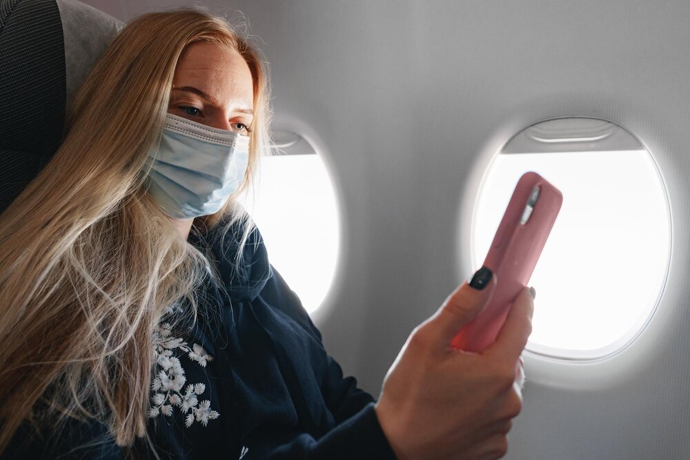 Young woman with long hair sitting in plane by the window and using smartphone